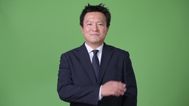 Mature Japanese businessman against green background — Stock Video