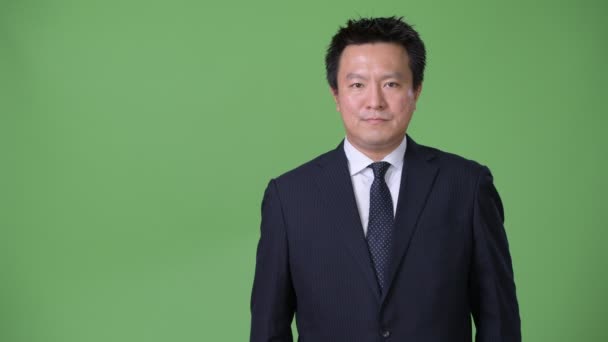 Mature Japanese businessman against green background — Stock Video