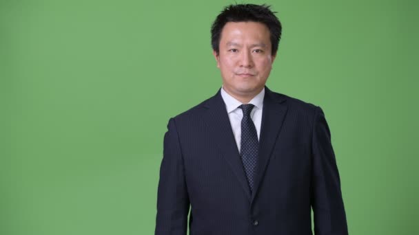 Mature Japanese businessman against green background — Stock Video