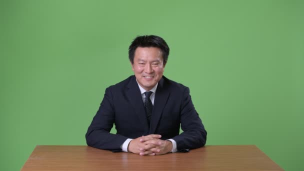 Mature Japanese businessman against green background — Stock Video