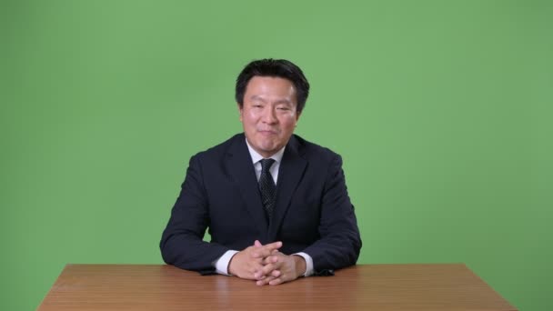 Mature Japanese businessman against green background — Stock Video