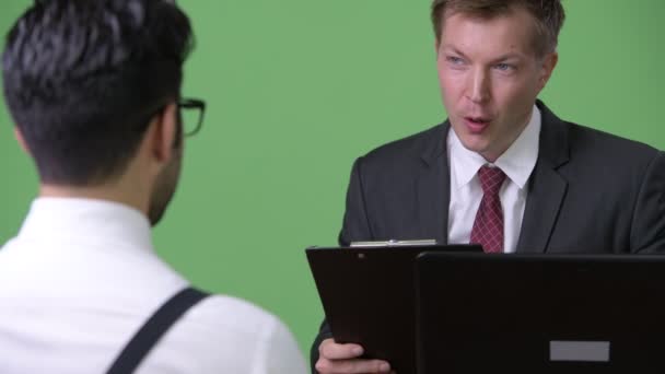 Два молодых многонациональных бизнесмена, работающих вместе на зеленом фоне — стоковое видео