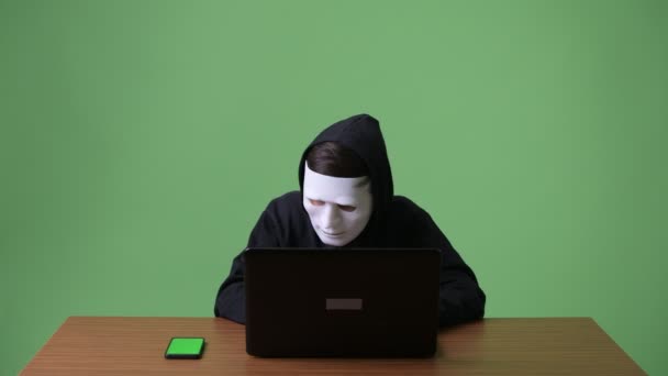 Jonge tiener computer hacker tegen groene achtergrond — Stockvideo