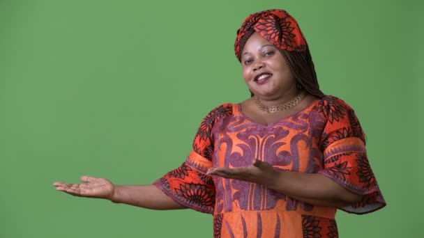緑の背景に対して伝統的な服を着ている太りすぎの美しいアフリカの女性 — ストック動画