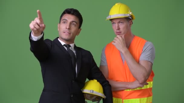 Multi-ethnic young businessman and young construction worker working together against green background — Stock Video