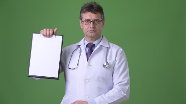 Mature handsome man doctor against green background — Stock Video