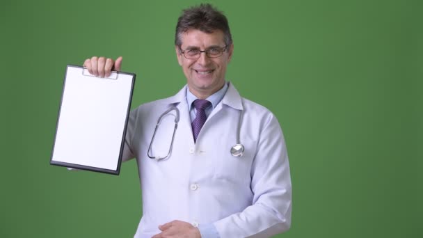 Ältere gut aussehende Mann Arzt vor grünem Hintergrund — Stockvideo