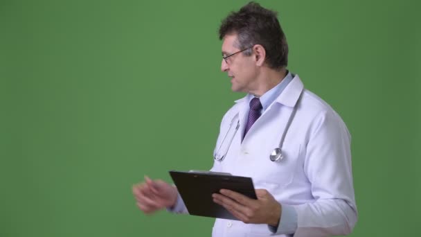 Ältere gut aussehende Mann Arzt vor grünem Hintergrund — Stockvideo