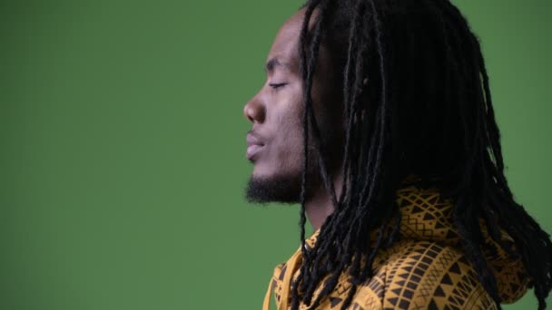 Young handsome African man with dreadlocks against green background — Stock Video