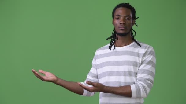 Young handsome African man with dreadlocks against green background — Stock Video