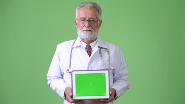 Handsome senior bearded man doctor against green background — Stock Video