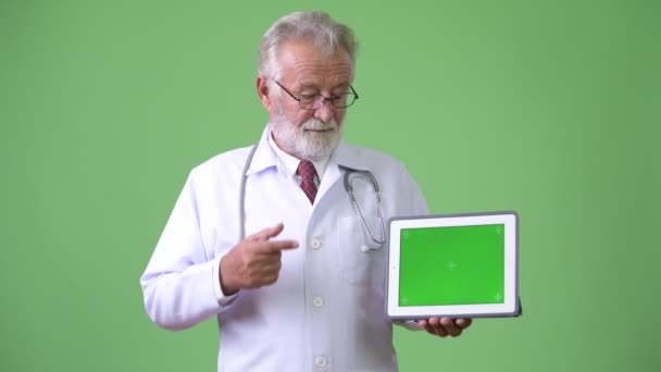 Bonito médico homem barbudo sênior contra fundo verde — Vídeo de Stock