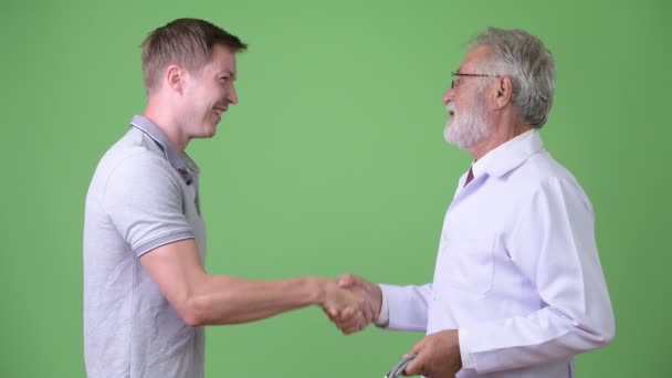 Senior barbudo hombre médico consultoría hombre paciente contra fondo verde — Vídeos de Stock