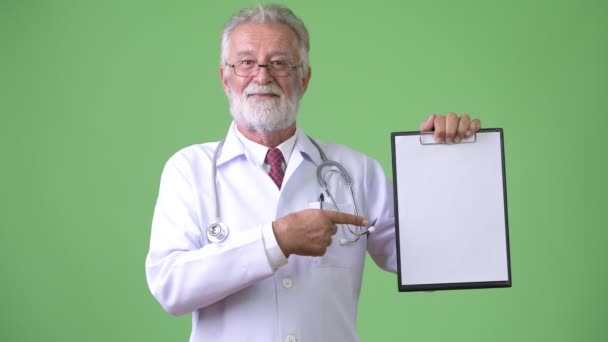 Bonito médico homem barbudo sênior contra fundo verde — Vídeo de Stock