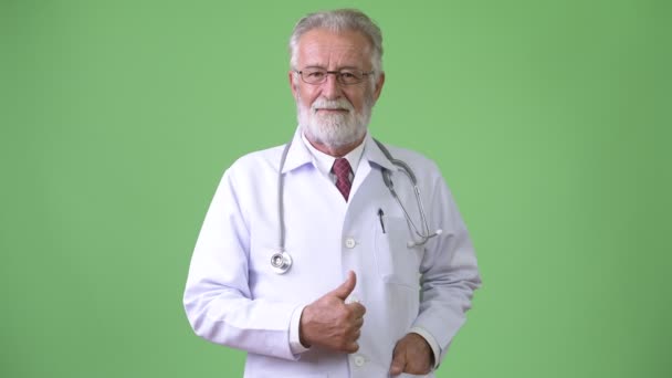 Handsome senior bearded man doctor against green background — Stock Video