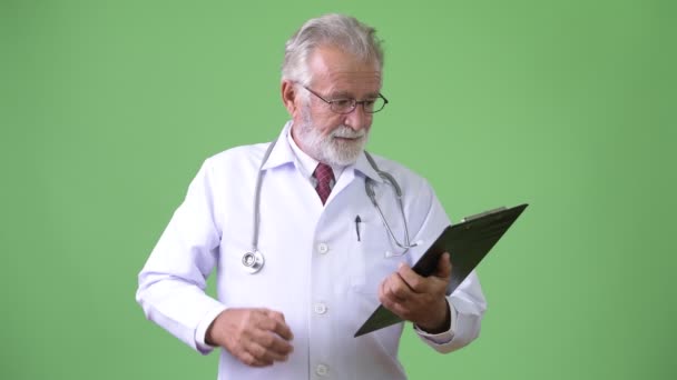 Handsome senior bearded man doctor against green background — Stock Video
