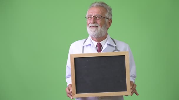 Handsome senior bearded man doctor against green background — Stock Video