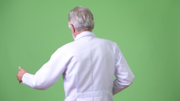 Handsome senior bearded man doctor against green background — Stock Video