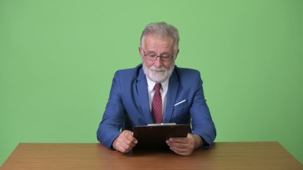 Handsome senior bearded businessman against green background — Stock Video