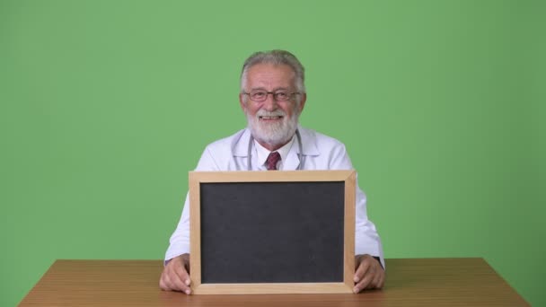 Handsome senior bearded man doctor against green background — Stock Video