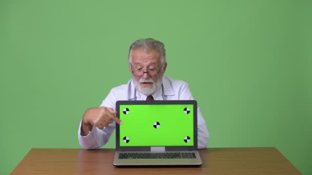 Handsome senior bearded man doctor against green background — Stock Video