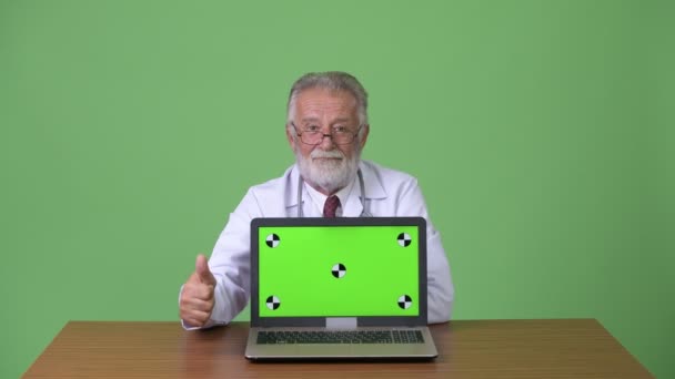 Handsome senior bearded man doctor against green background — Stock Video