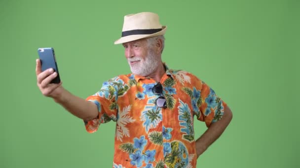 Handsome senior bearded tourist man ready for vacation against green background — Stock Video