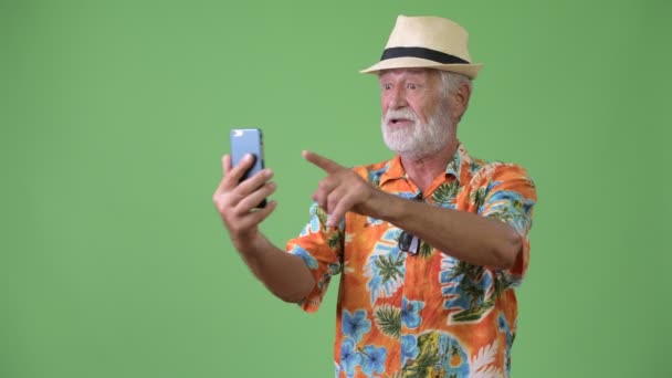 Handsome senior bearded tourist man ready for vacation against green background — Stock Video