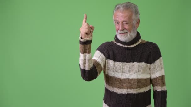 Knappe senior bebaarde man het dragen van warme kleding tegen groene achtergrond — Stockvideo