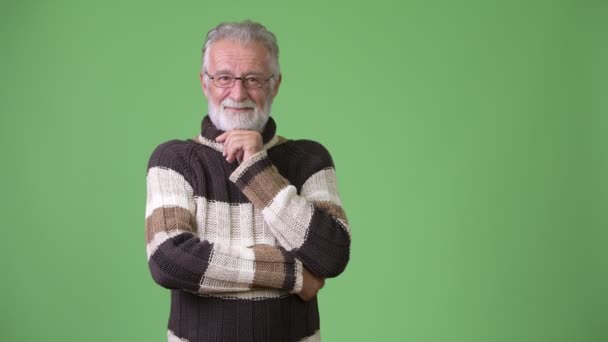 Bel homme barbu senior portant des vêtements chauds sur fond vert — Video