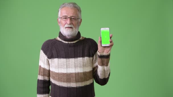 Красивий старший бородатий чоловік у теплому одязі на зеленому тлі — стокове відео