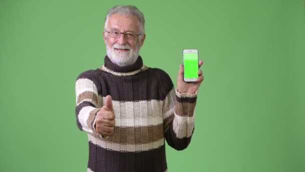 Handsome senior bearded man wearing warm clothing against green background — Stock Video