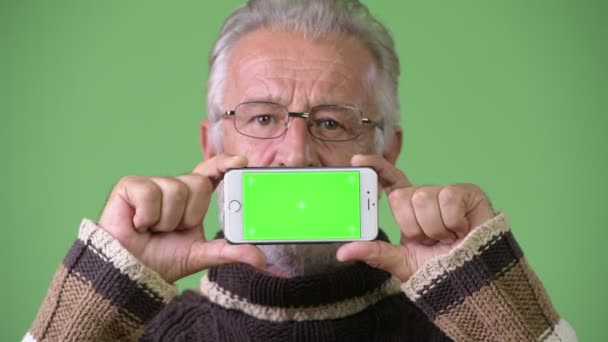 Knappe senior bebaarde man het dragen van warme kleding tegen groene achtergrond — Stockvideo