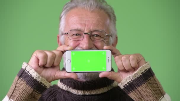 Knappe senior bebaarde man het dragen van warme kleding tegen groene achtergrond — Stockvideo