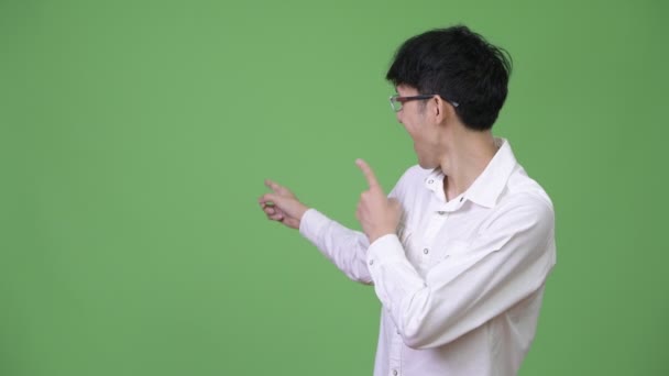 Junge glückliche asiatische Geschäftsmann zeigt auf den Rücken — Stockvideo