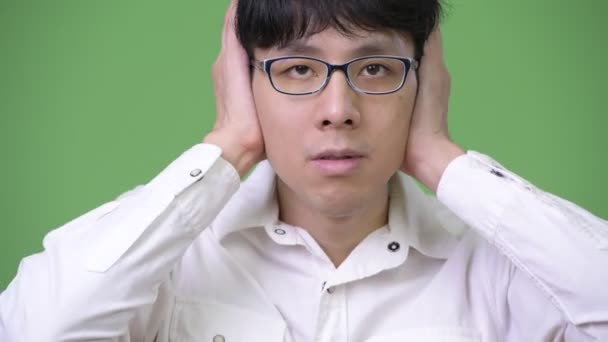 Молодой азиатский бизнесмен прикрывает уши, так как не слышит злого понятия — стоковое видео