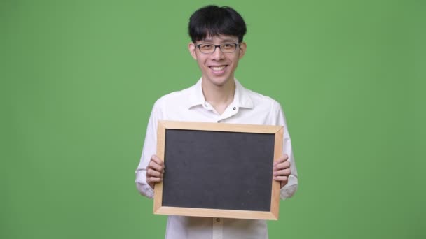 Χαρούμενος νεαρός επιχειρηματίας Ασίας χαμογελώντας κρατώντας μαυροπίνακα — Αρχείο Βίντεο