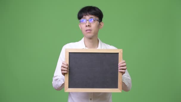 Young Asian businessman holding blackboard while thinking — Stock Video