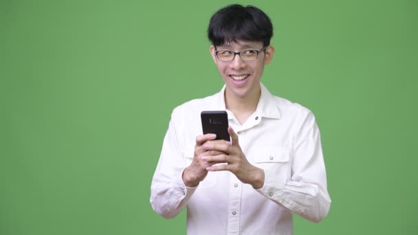 Happy young Asian businessman smiling while using phone and thinking — Stock Video