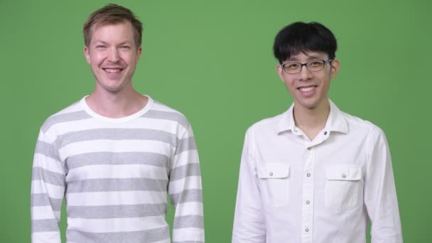 Двоє молодих багатоетнічних бізнесменів посміхаються разом на зеленому фоні — стокове відео