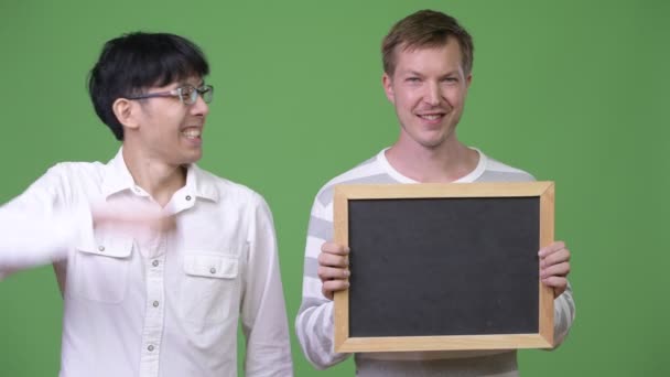 Two happy young multi-ethnic businessmen showing blackboard and giving thumbs up — Stock Video