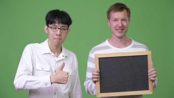 Zwei glückliche junge multiethnische Geschäftsleute zeigen Tafel und geben Daumen hoch — Stockvideo