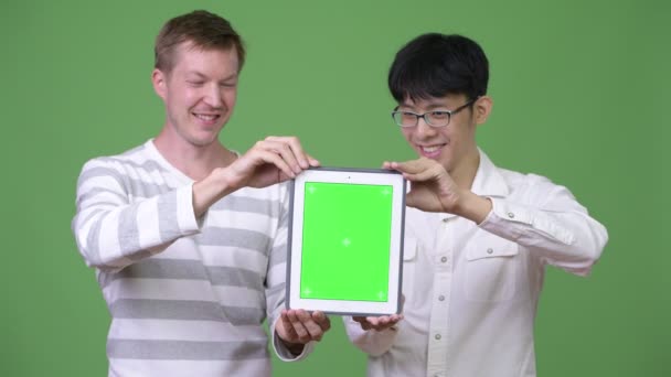 Два счастливых молодых мультиэтнических бизнесмена вместе показывают цифровой планшет на камеру — стоковое видео