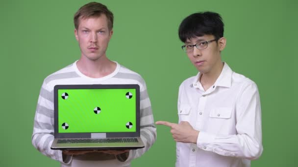 Zwei junge multiethnische Geschäftsleute zeigen Laptop in die Kamera, während sie mit dem Finger zeigen — Stockvideo