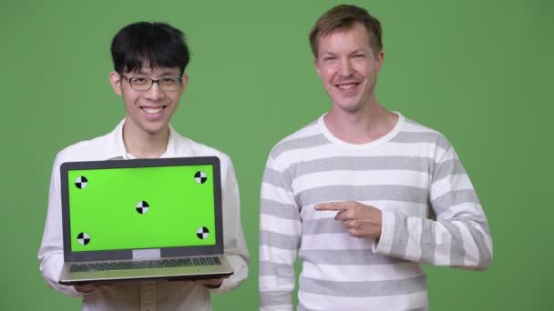 Два молодых многонациональных бизнесмена, показывающих ноутбук на камеру, указывая пальцем — стоковое видео