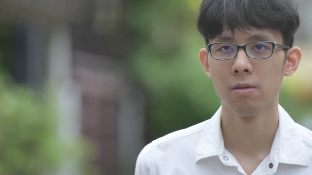 Fiatal boldog ázsiai üzletember, mosolyogva, miközben gondolkodás az utcán szabadban — Stock videók