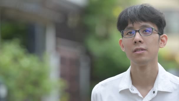 Fiatal boldog ázsiai üzletember, mosolyogva, miközben gondolkodás az utcán szabadban — Stock videók