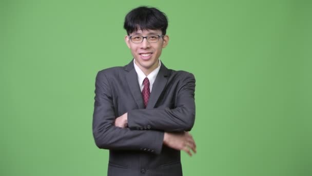 Молодой счастливый азиатский бизнесмен улыбается со скрещенными руками — стоковое видео