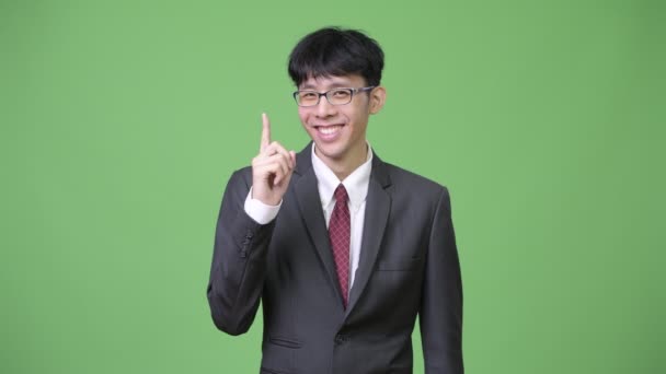 Молодой азиатский бизнесмен улыбается, показывая пальцем вверх — стоковое видео