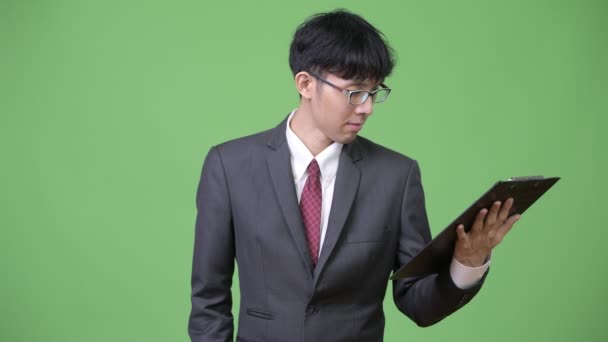 Young Asian businessman reading and thinking with clipboard — Stock Video